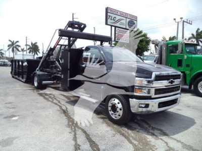Front-left view of a new 2023 Chevrolet Silverado 6500HD truck with a heavy-duty dumping bed and hoisting mechanism, dealership lot in background.