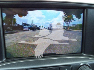 Dashboard/instrument cluster viewpoint showing rear-view mirror display with a circular road-work symbol overlay and outdoor lot reflection.