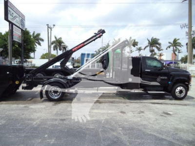 Chevrolet Silverado 6500HD tow truck side view showing tow boom and hydraulic winch, black cab and white body with Silverado branding, palm trees in background.