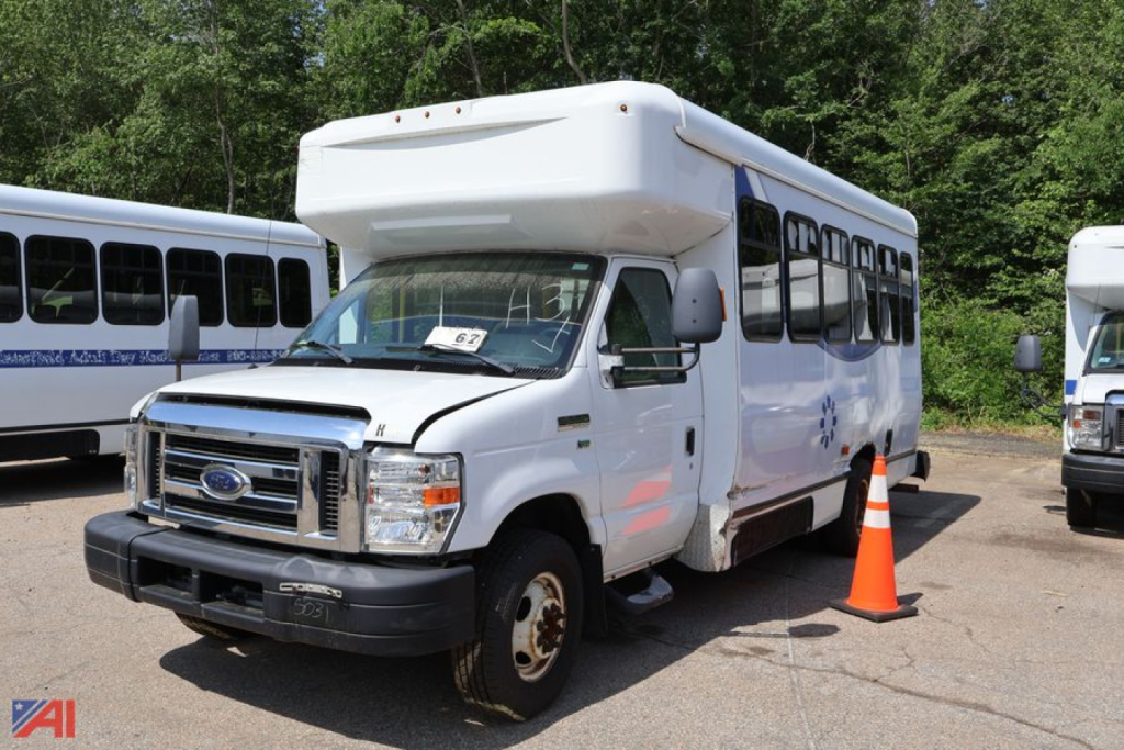 Ford E-350 wheelchair bus body with raised roof, front grille, headlights, and orange traffic cone nearby.