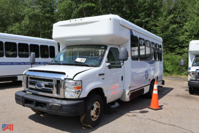 Ford E-350 wheelchair bus body with raised roof, front grille, headlights, and orange traffic cone nearby.