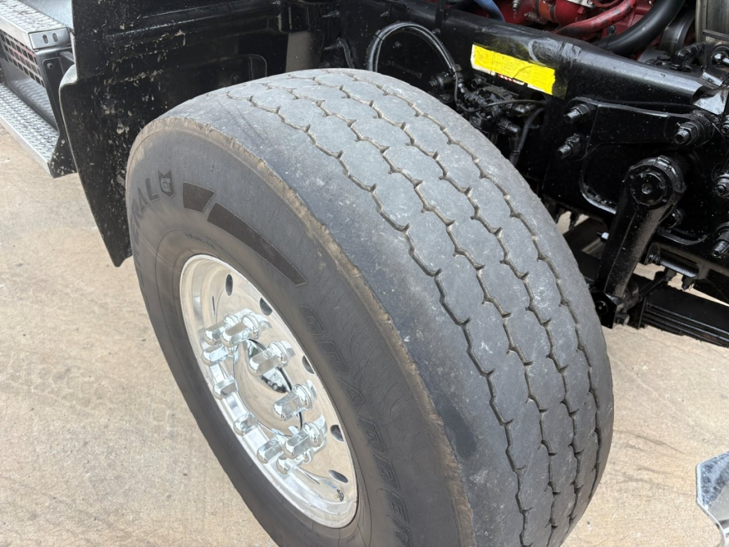 Front left tire and undercarriage of a 2020 Mack GR64F dump truck showing tire tread and chrome wheel.