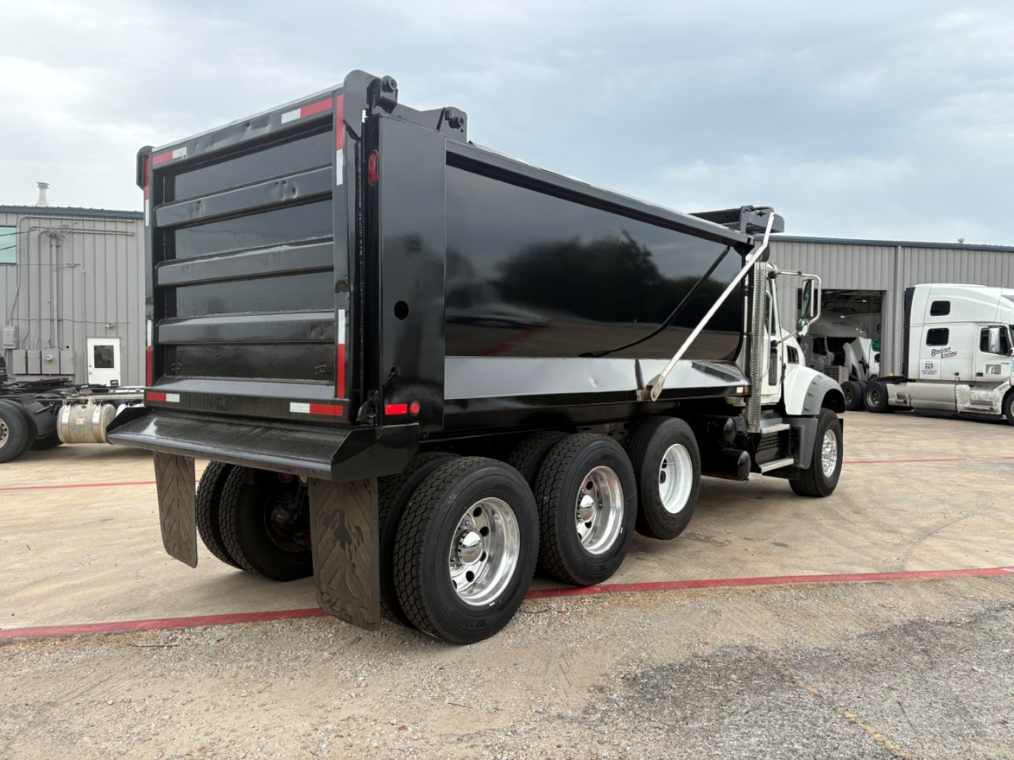 Dump truck rear and side view showing a black dump body on a Mack GR64F chassis with tandem rear axles.