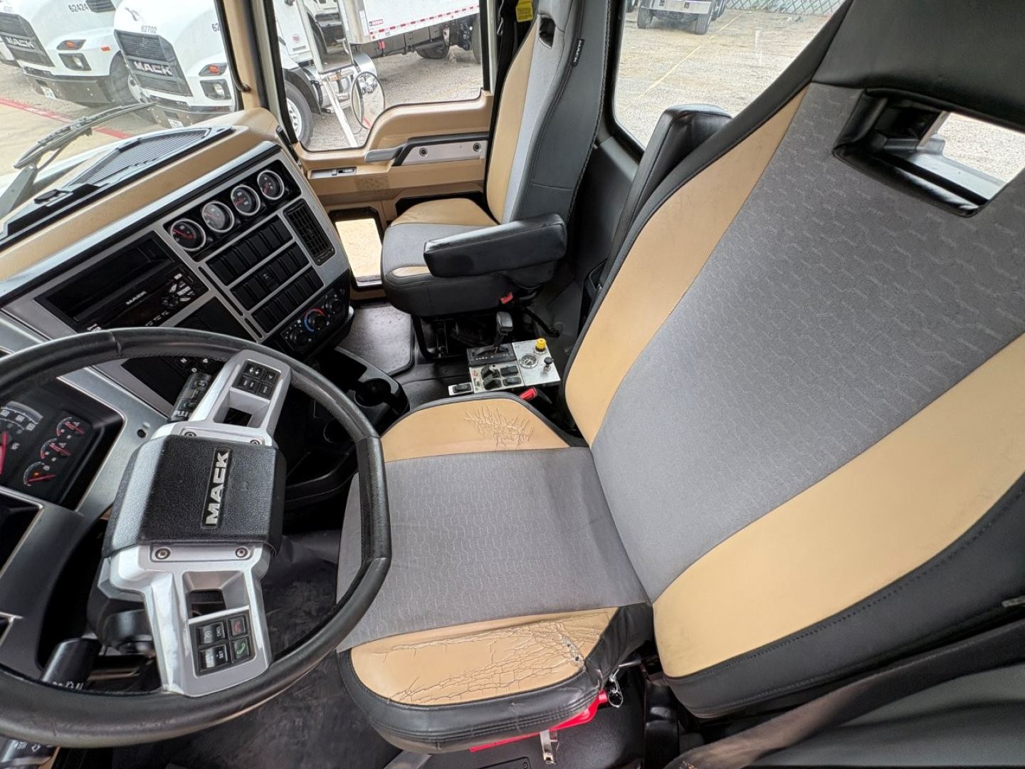 Cab interior of a 2020 Mack GR64F dump truck showing steering wheel, dashboard with gauges, and two-tone seats in gray and tan.