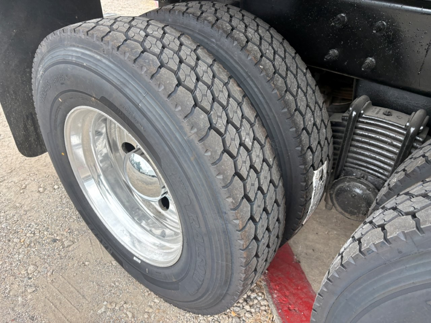 Front dual rear tire view of a Mack GR64F dump truck showing dual rear wheels and suspension components.