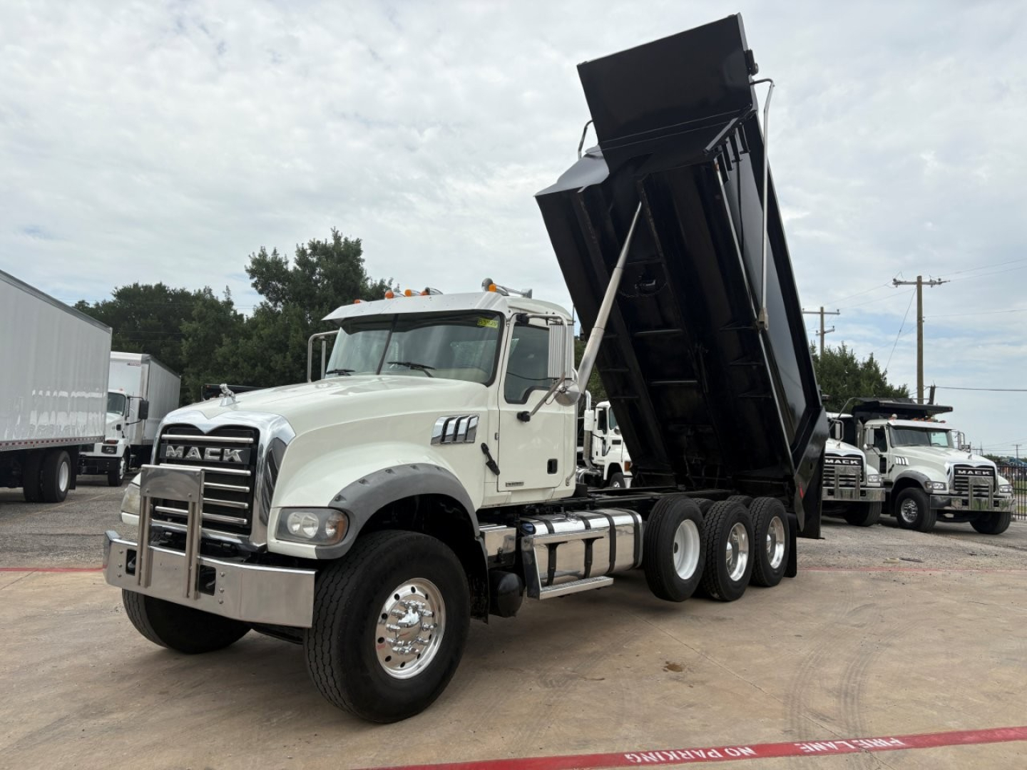 Mack GR64F dump truck in-tilt position showing front grille with Mack lettering and dual rear wheels, white cab, black dump body raised, dealership lot background.