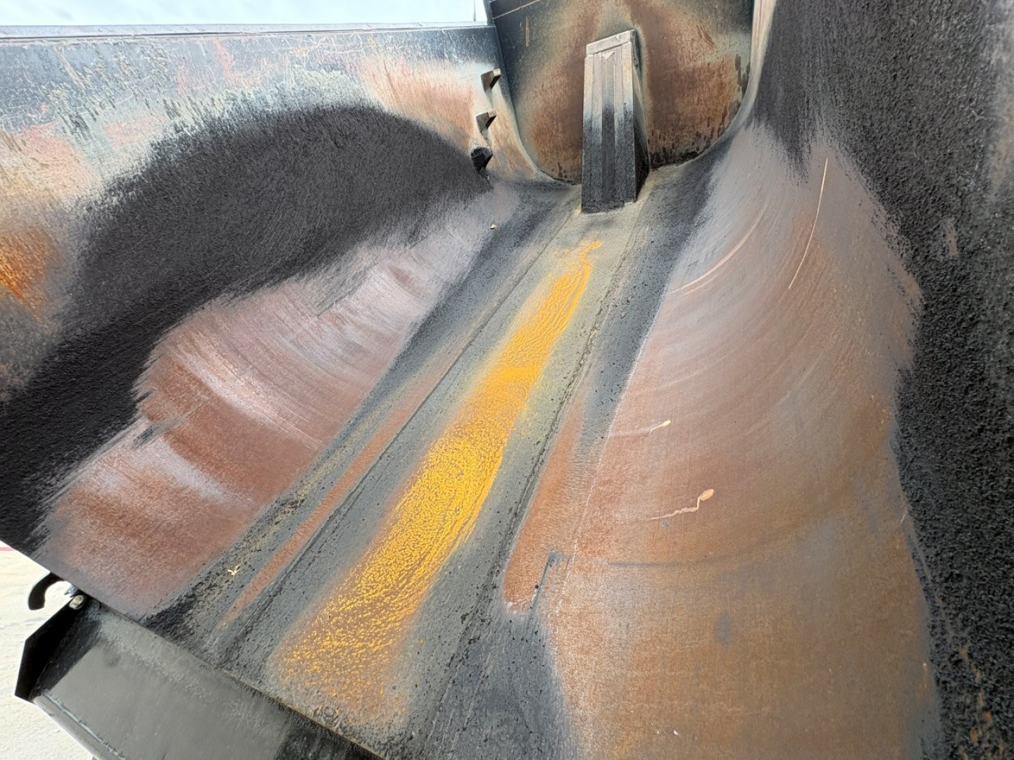 Dump truck bed interior with painted yellow line and metal surfaces, showing rust-colored patches and wheel area