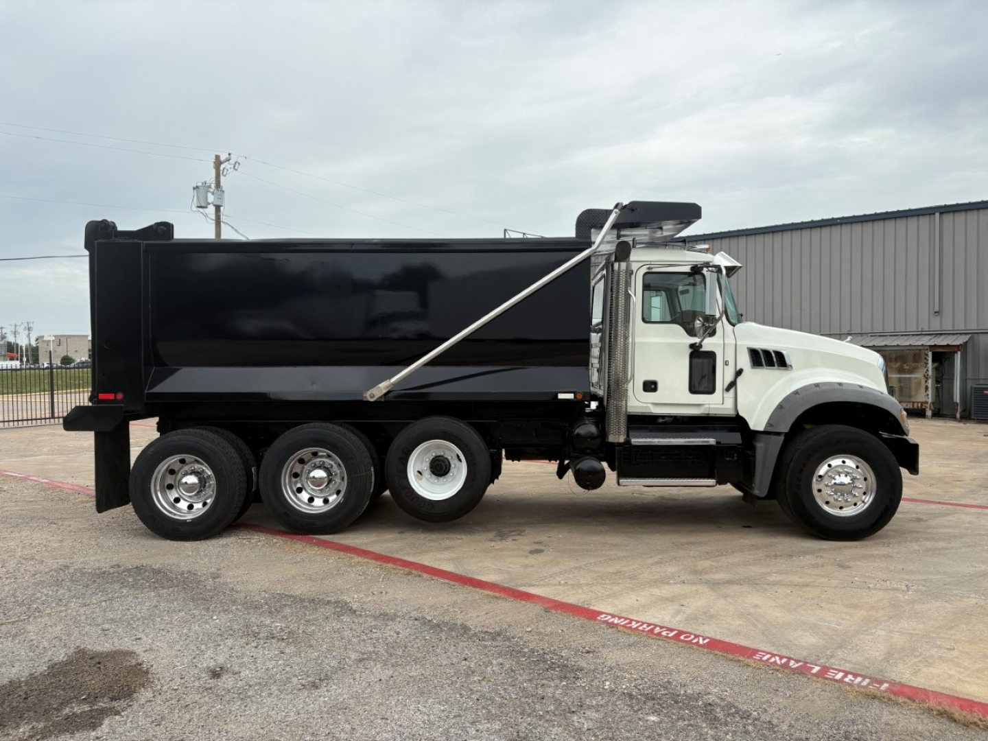 Dump truck side view showing black dump body on white cab with six wheels and hydraulic dump mechanism.
