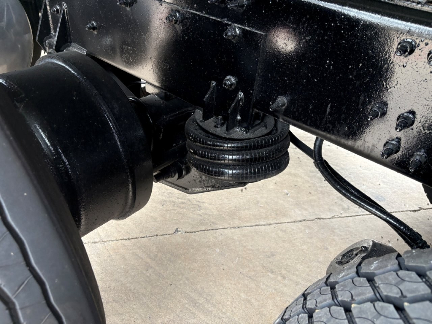 Rear underside of a 2020 Mack GR64F chassis showing a lifting mechanism and suspension components with a black painted frame.