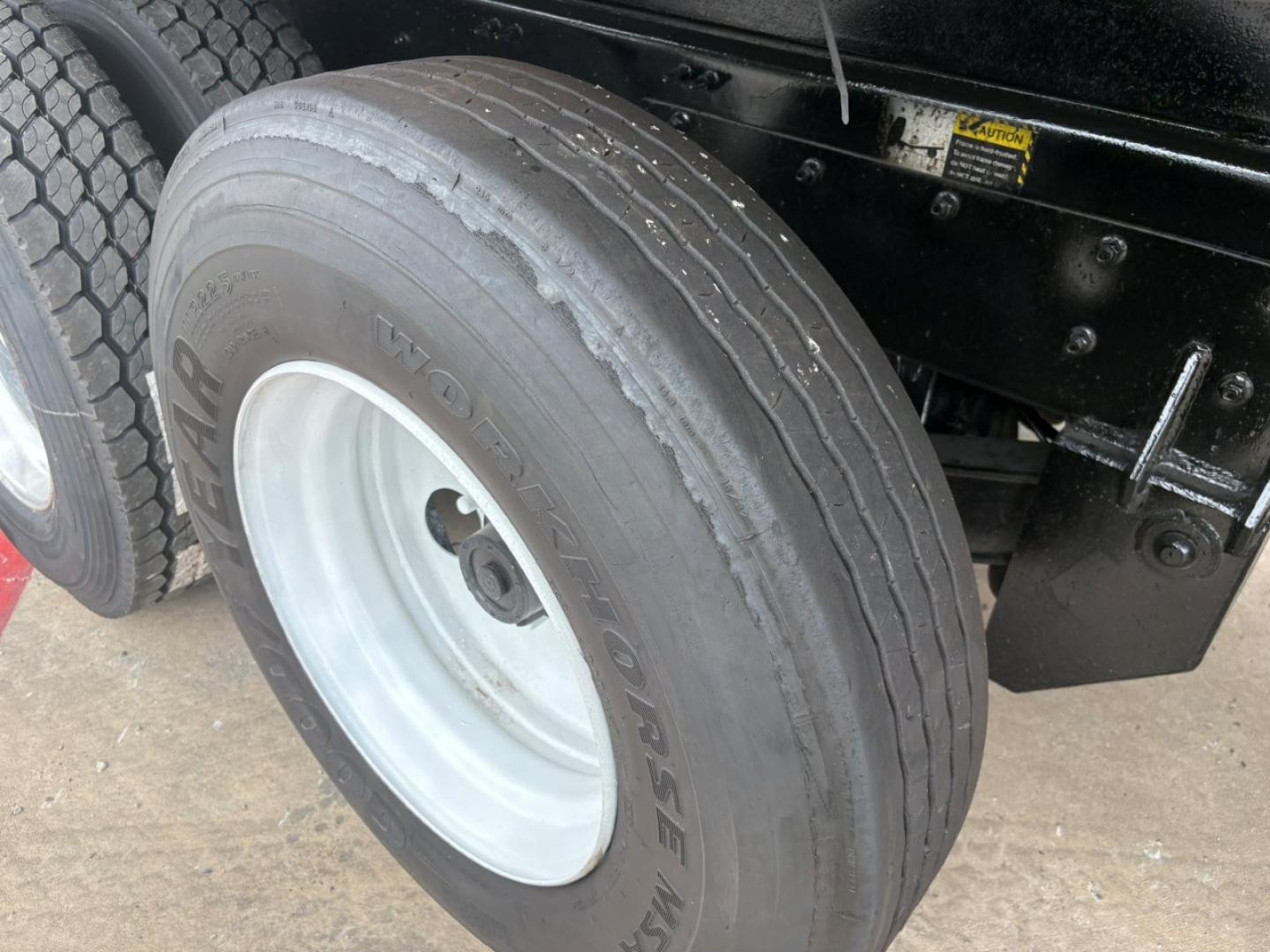 Tire and wheel of a 2020 Mack GR64F dump truck showing Goodyear tire on steel rim and part of chassis with warning label.