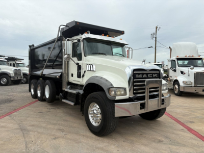 Mack GR64F dump truck in light green with black dump body, showing front grille with 'MACK' lettering, dual rear axles, chrome bumper guard, and side steps. No visible license plate text.