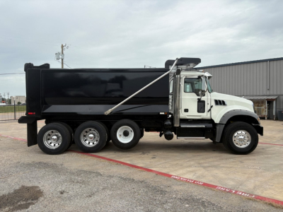 Dump truck side view showing black dump body on white cab with six wheels and hydraulic dump mechanism.