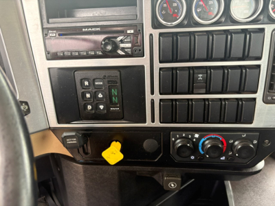 Mack GR64F interior dash showing gear selector with N and mode buttons, audio head unit, multiple gauges, climate controls, and yellow key tag.