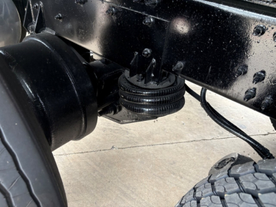 Rear underside of a 2020 Mack GR64F chassis showing a lifting mechanism and suspension components with a black painted frame.