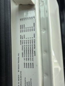 VIN plate on Mack GR64F showing GVWR and GAWR weights and axle specs in a vertical orientation.