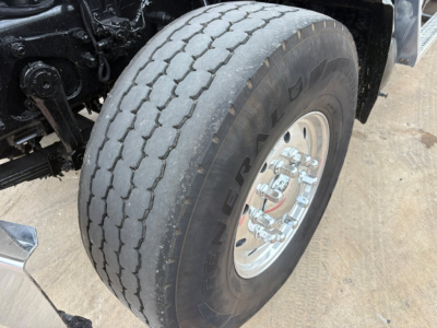 Truck wheel and tire close-up showing heavy-duty dual rear axle with Alliance wheel, curb lean and tire tread pattern.
