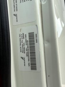 Mack Trucks VIN plate and label text on vehicle frame showing VIN 1M2GR4GC9LM016749 and stock number B3428P in a dump truck setup.