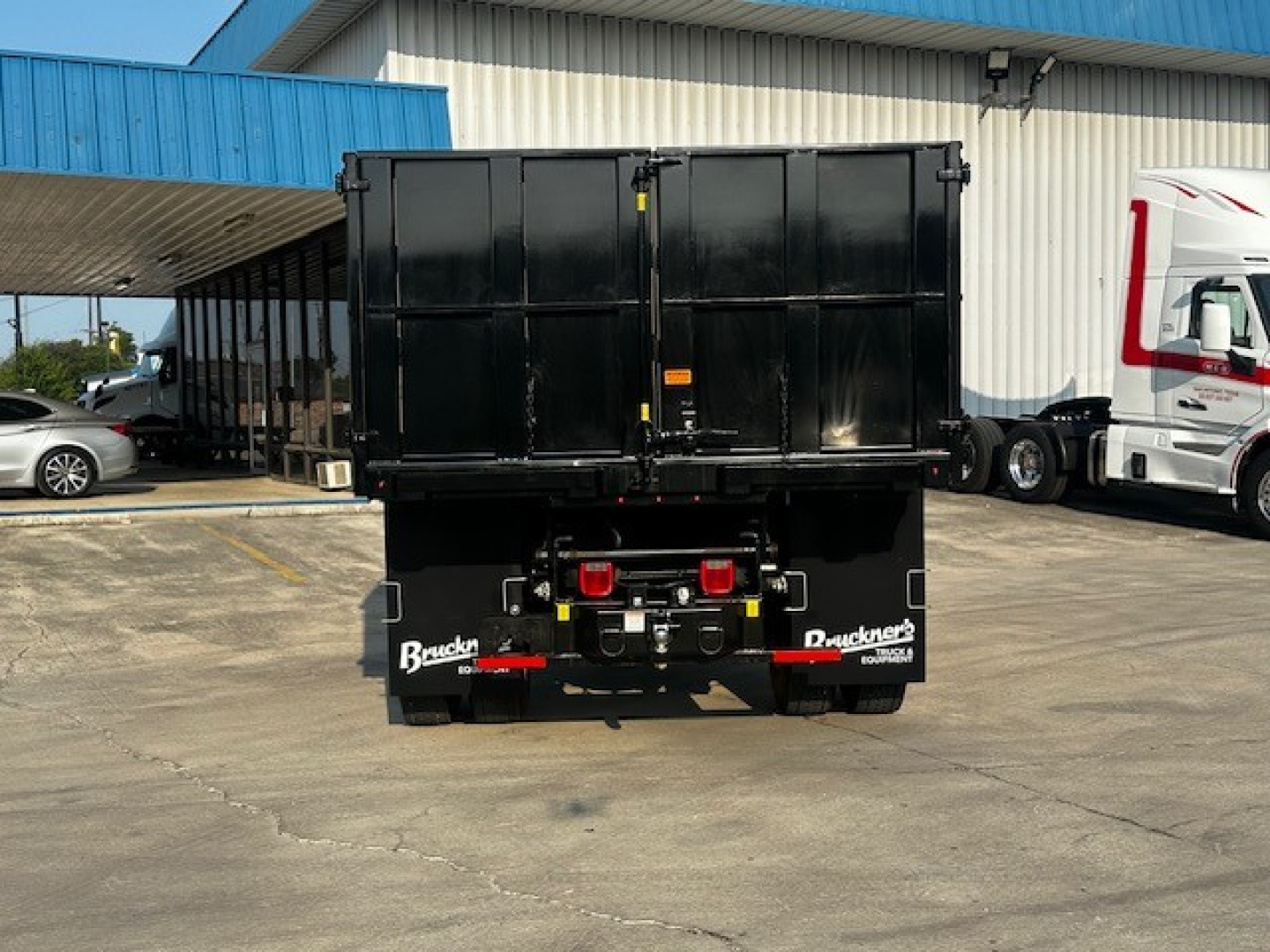 Rear view of a black dump truck bed with Buckeye branding on mudflaps, hydraulic connections, and rear lights.
