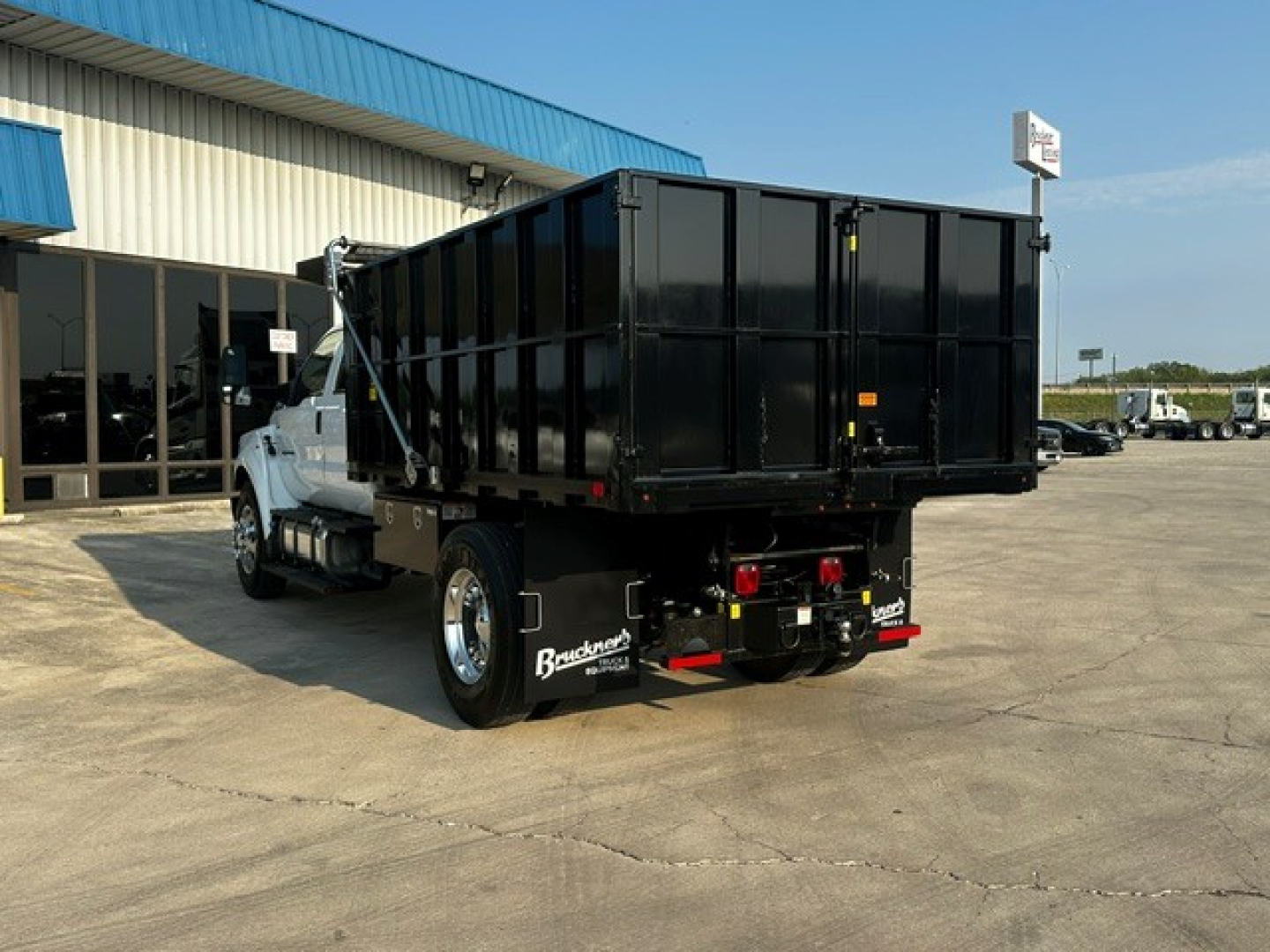 Dump truck from rear-left side showing large black dump bed and white cab, Ford F-750, in a dealership lot.