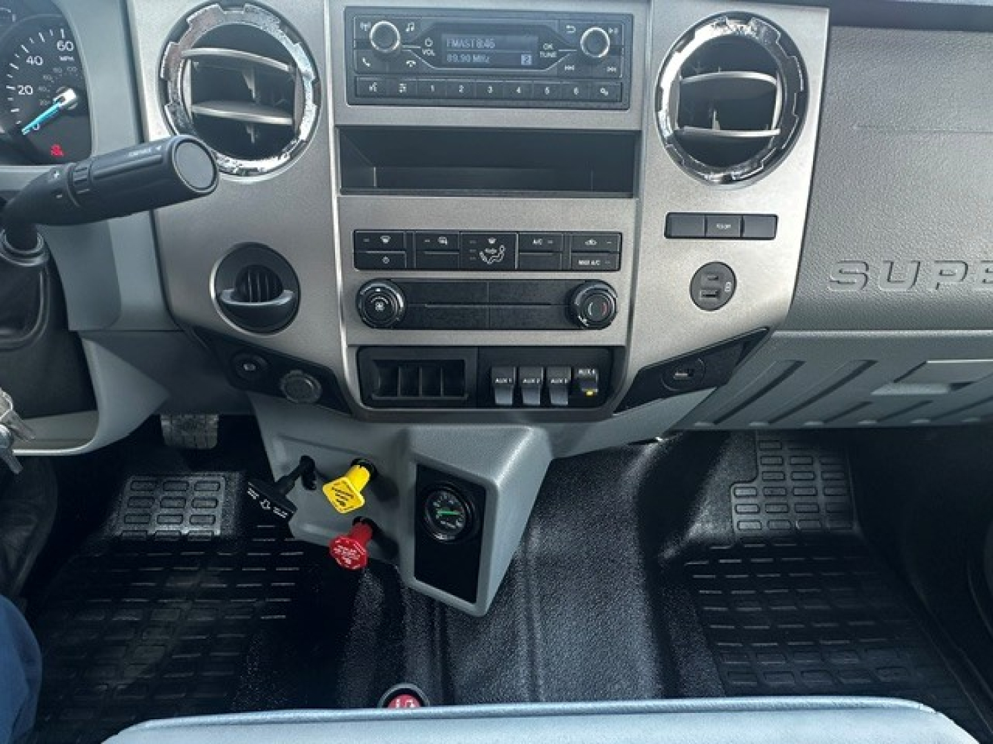 Dashboard of a Ford F-750 dump truck showing center stack with radio, climate controls, two circular air vents, and ignition area; yellow and red keys and gauges visible.