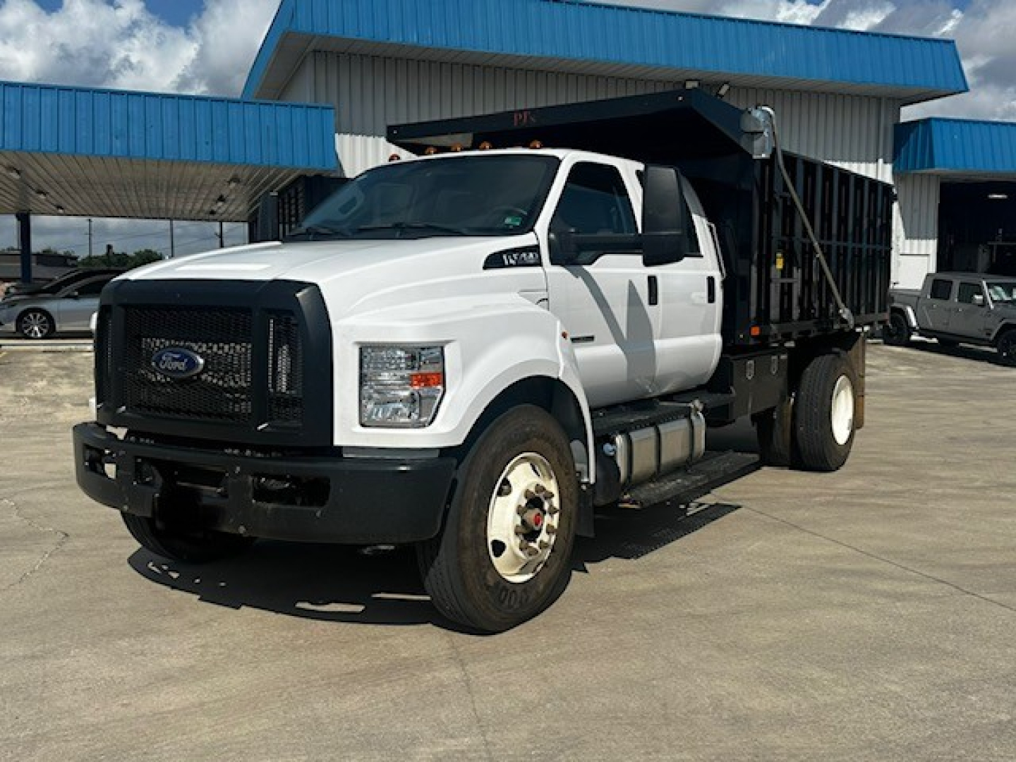 Ford F-750 dump truck in white with black dump bed, side view showing cab and front grille.