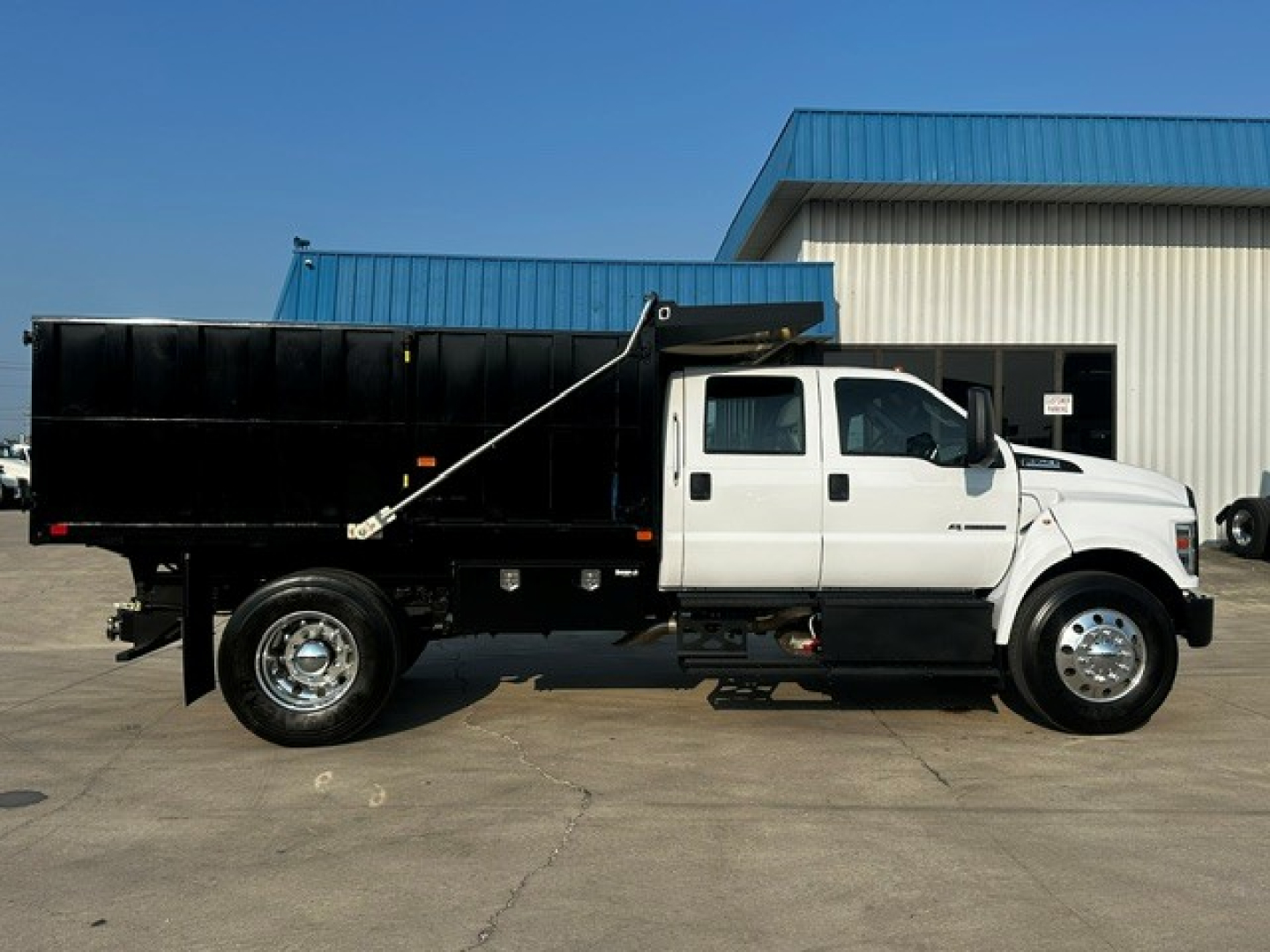 Side view of a white Ford F-750 dump truck with a black dump bed parked in front of a building.