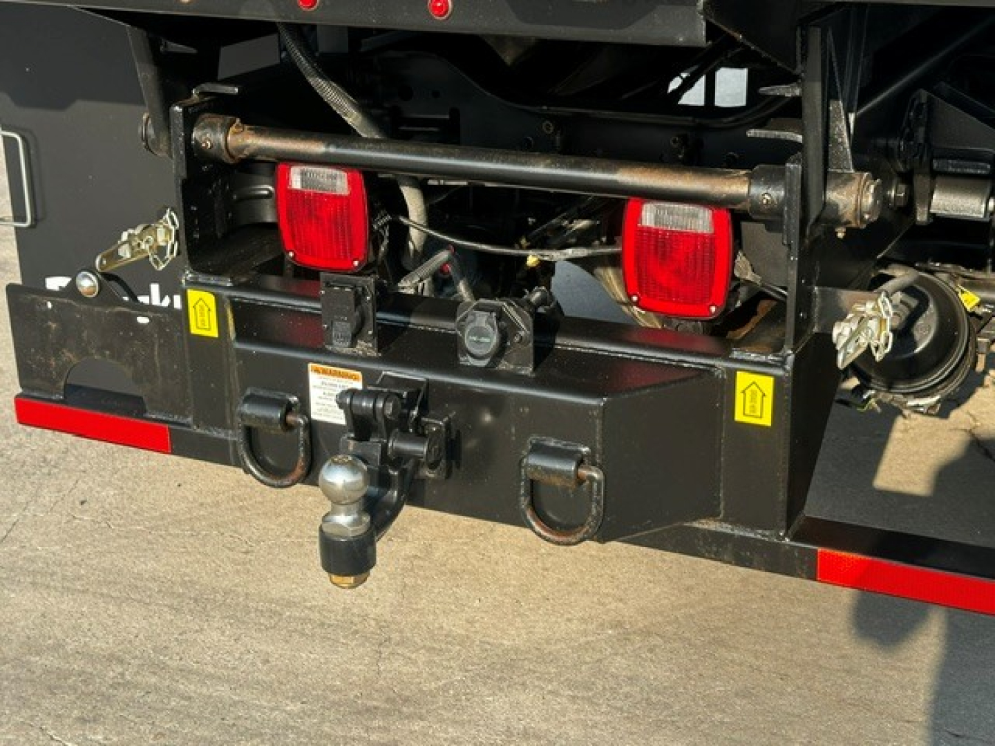 Rear view of Ford F-750 dump truck showing tow hitch, rear lights, and warning decals on bumper.