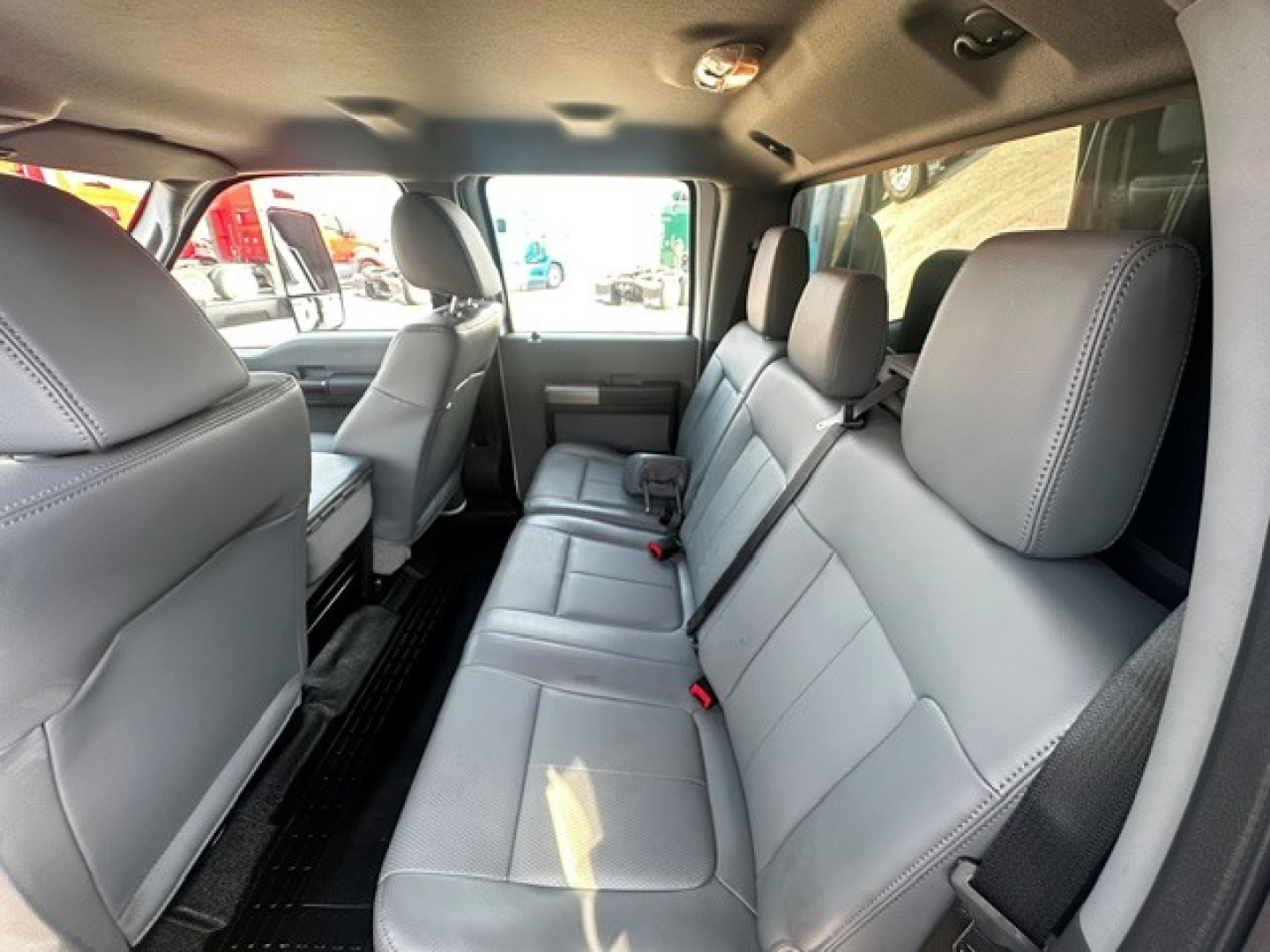 Truck interior showing rear bench seat with gray leather upholstery and three seat belts; front and back seats visible with headrests; cabin area with overhead lights.