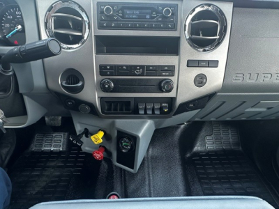 Dashboard of a Ford F-750 dump truck showing center stack with radio, climate controls, two circular air vents, and ignition area; yellow and red keys and gauges visible.