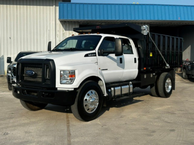 White Ford F-750 dump truck in daytime, front three-quarter view, with black grille guard and dump bed, side mirrors, and dual rear wheels.