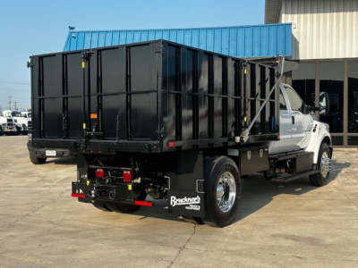 Dump truck chassis with a black dump bed on a white Ford F-750 cab and chassis; rear view showing hitch, taillights, and hydraulic dump mechanism.
