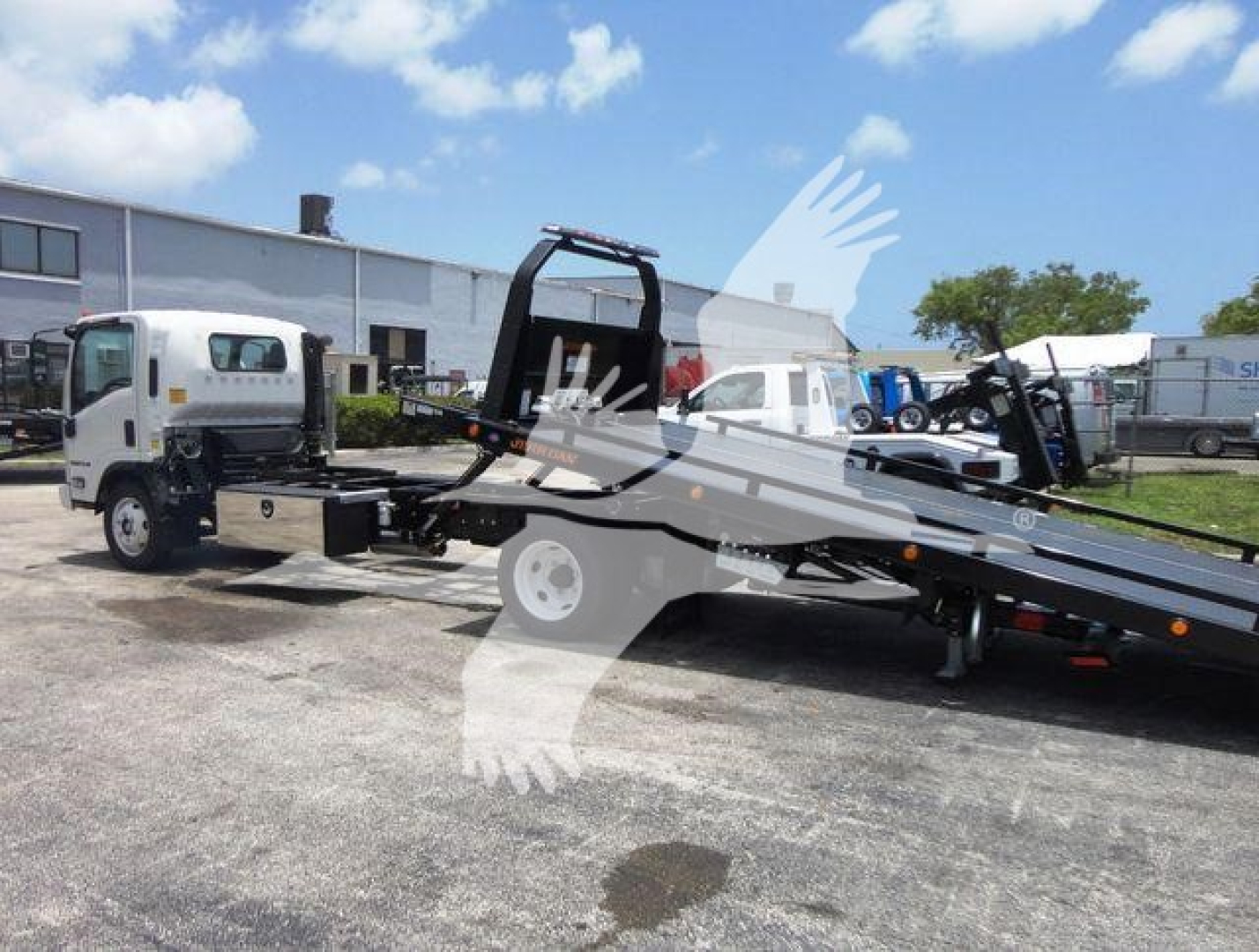 Isuzu NRR rollback tow truck with flatbed in-service, side view showing empty cab and wheeled hydraulic winch, text on trailer and truck not fully legible.