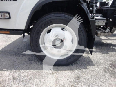 Isuzu NPRR rollback truck front wheel and tire showing white hubcap and partial suspension/steering components; portion of the chassis and wheel well visible.
