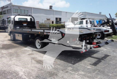 Isuzu NRRGAS21RRSB rollback truck on a flatbed trailer with hydraulic ramps, in-service equipment yard, front of truck visible, stock number NRRGAS21RRSB.