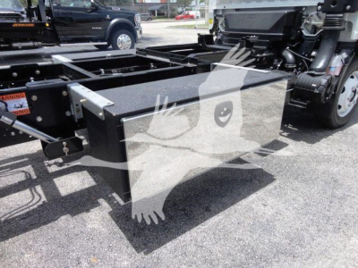 Isuzu NRR rollback truck chassis with a large rectangular metal toolbox mounted between the frame rails; visible components include a black toolbox, frame rails, and part of the cab suspension.