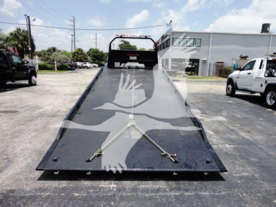 Isuzu rollback truck bed with loading ramp and straps in view.