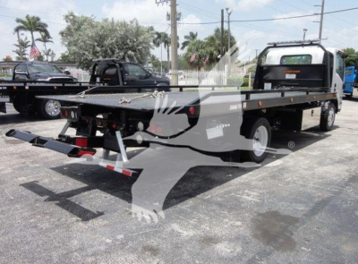 Isuzu NPRR rollback truck in a dealership lot showing flatbed with ramps and dual rear wheels.