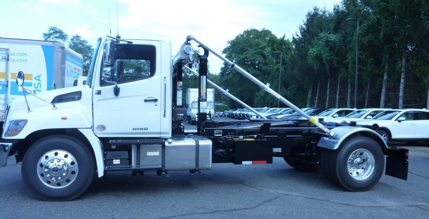 Truck chassis with hook lift mechanism, cab and wheelbase visible. Side shows Hino badge and fuel tanks; no legible small text.