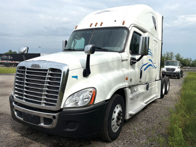 Truck cab of a white Freightliner Cascadia125 semi-truck with large grille, side mirrors, and blue decorative graphics; visible windows and front bumper