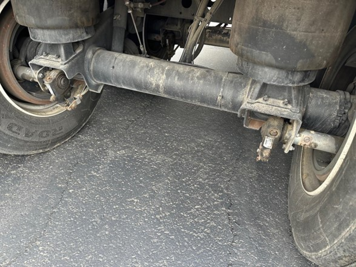 Rear underside of trailer showing axles, suspension, and frame with piping; no legible text visible.