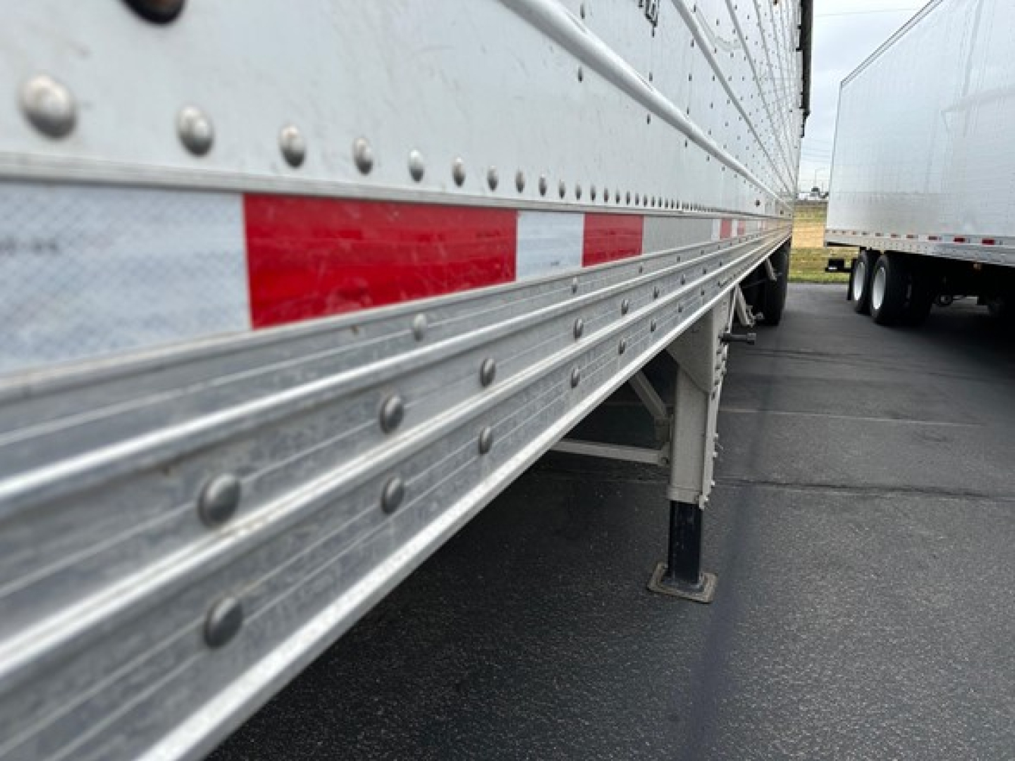 Trailer side view showing riveted metal hopper body and support legs with red-and-white reflective tape