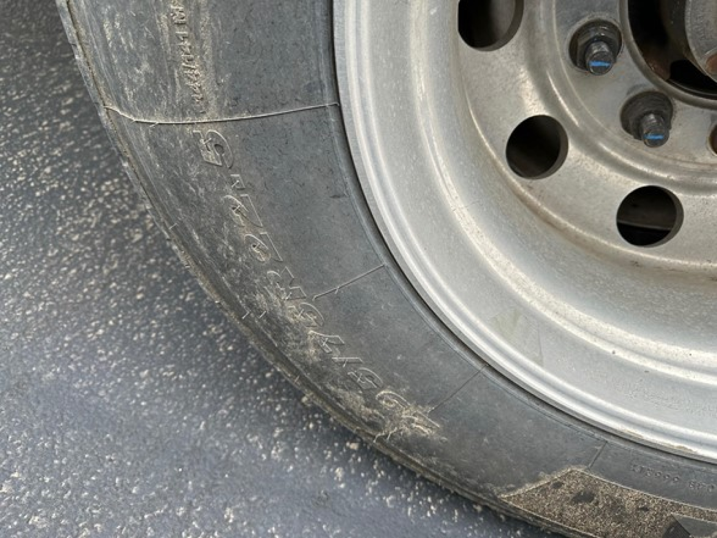 Tire sidewall and wheel of a trailer showing partial tread and stamped rim holes; no legible model text visible.