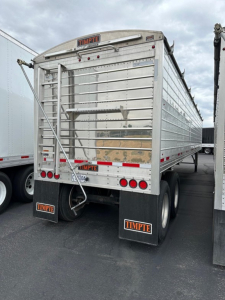 Timpte Super Hopper trailer rear view showing metal side panels, ladder, taillights, rear bumper, and TIMPTE mudflaps.