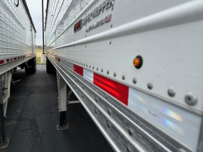 Timpte Super Hopper trailer side profile showing riveted aluminum walls, safety reflective tape, and support leg near the ground.