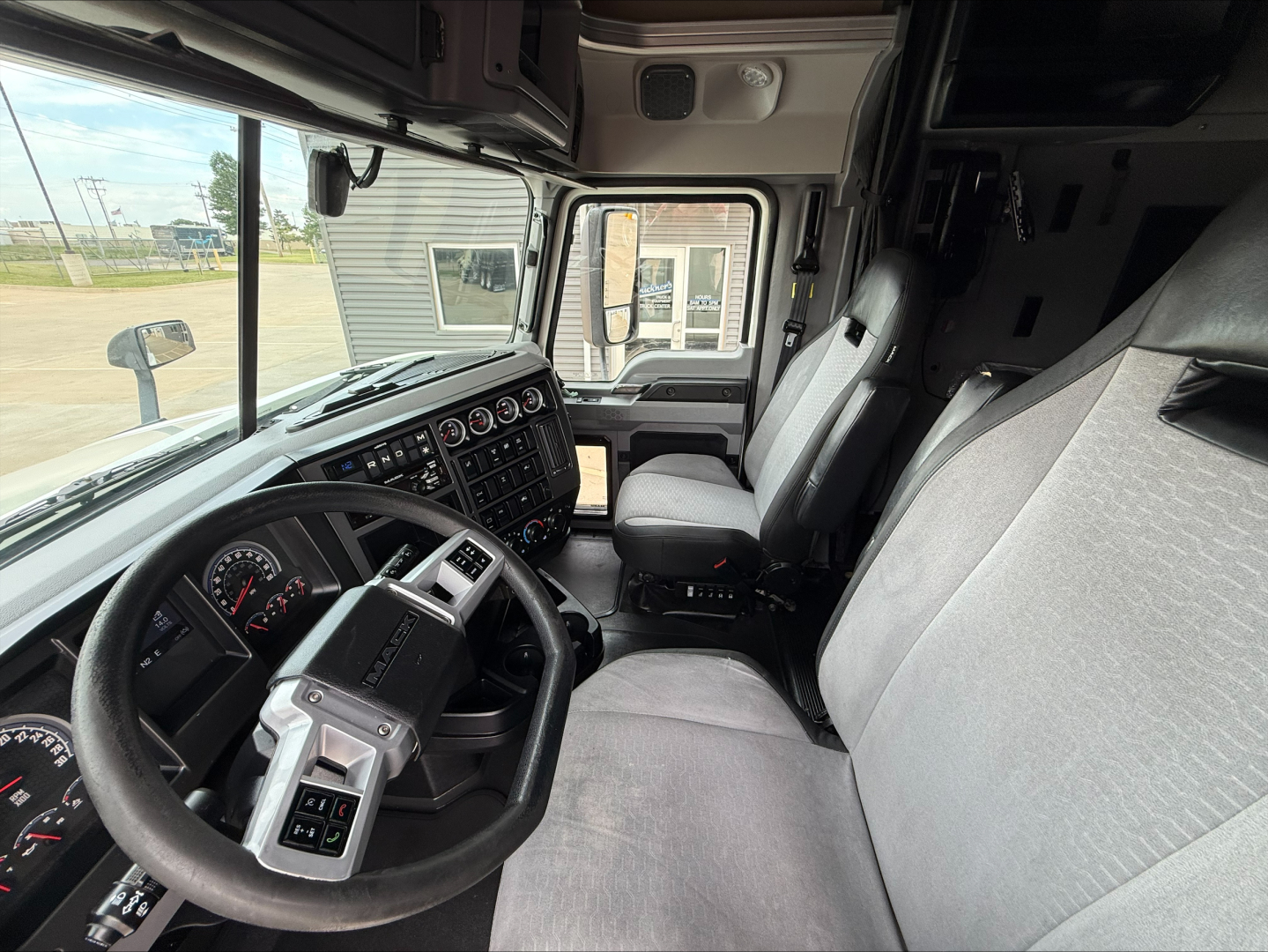 Interior of a 2020 Mack Anthem tractor cab showing steering wheel, dashboard with gauges, and front seats with light gray fabric.