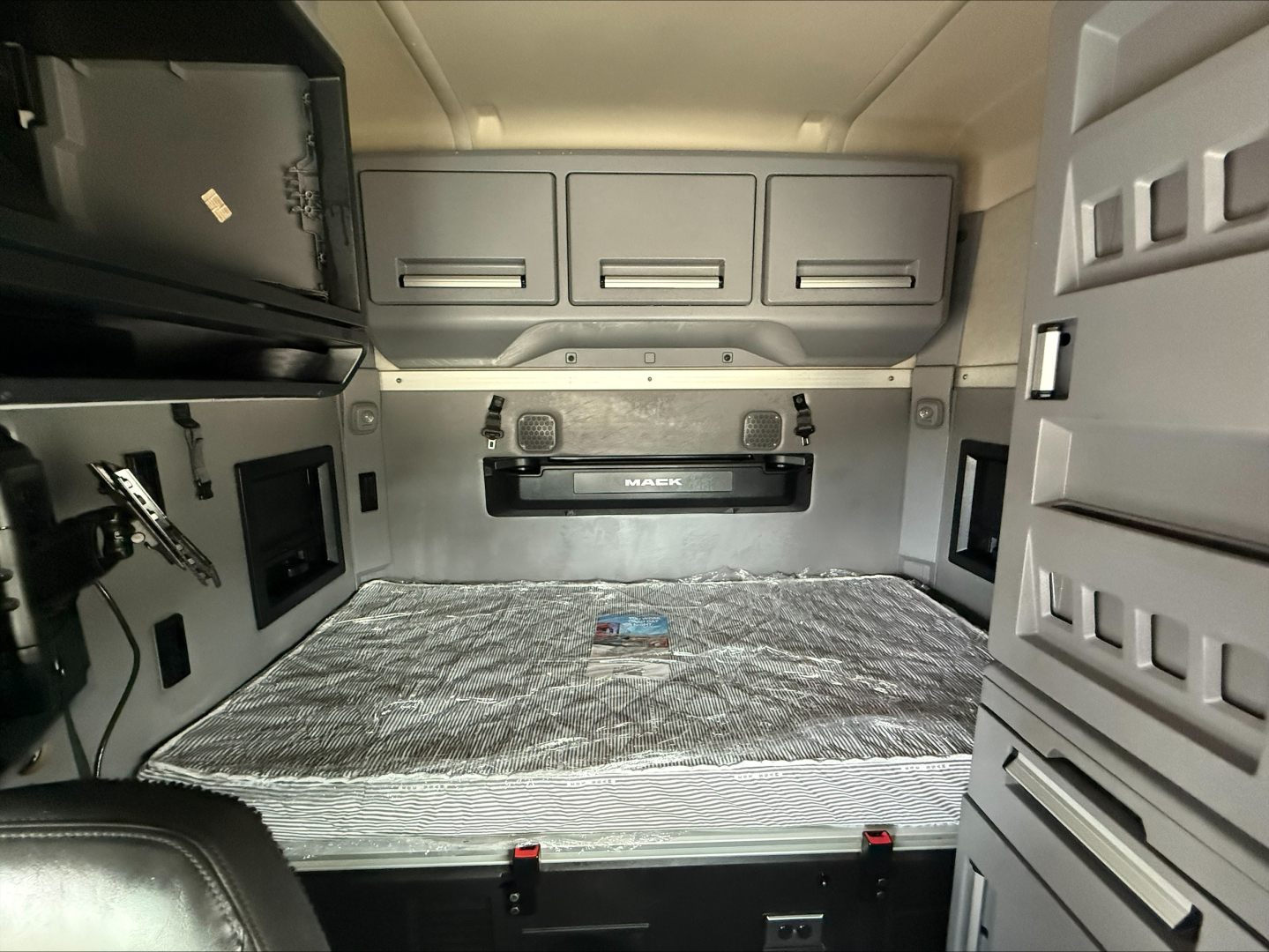 Tractor-trailer sleeper cab interior showing bed area with storage cabinets and control panels.