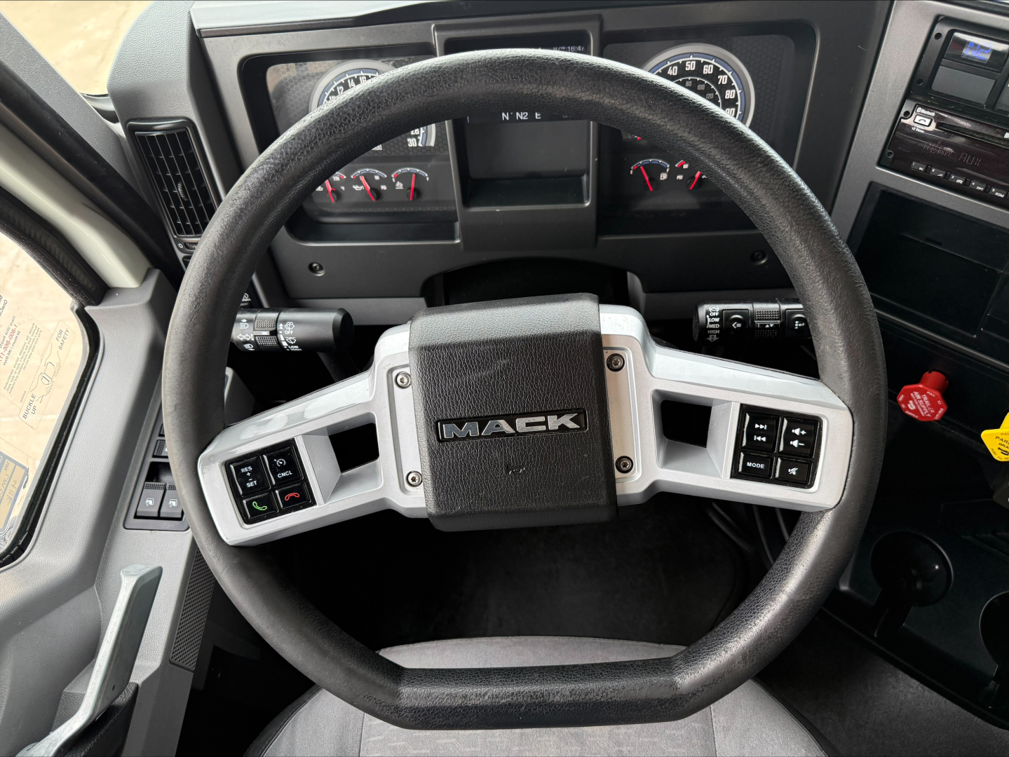 Mack steering wheel inside a truck cab with gauges and controls visible, center of wheel shows 'MACK' emblem.