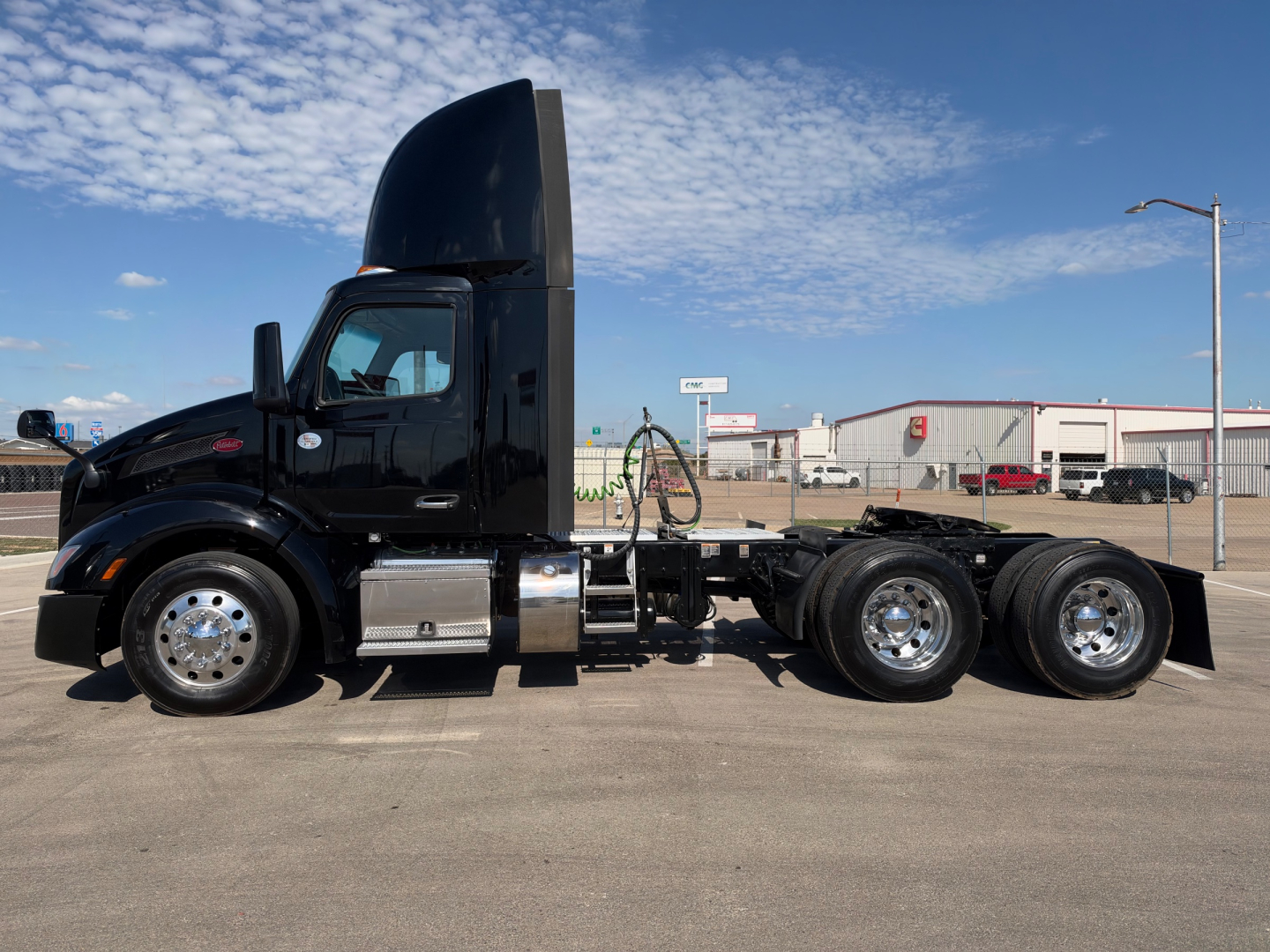 Peterbilt 579 conventional daycab tractor side view showing cab, white fuel tanks, dual rear axles, black paint, and tall sleeper-less hood with chrome steps.