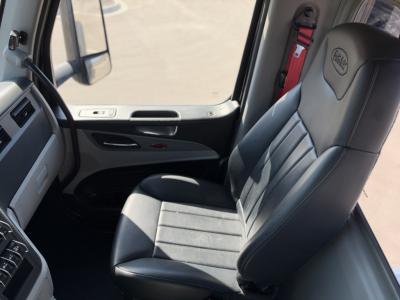 Peterbilt 579 cabin interior view showing driver seat and door panel with black leather seat, steering column and dashboard edge in a truck cab.