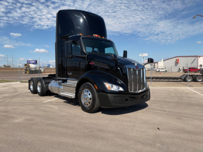Peterbilt 579 truck in a parking lot, black with a raised sleeper, large chrome grille, and dual rear axles.